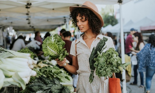 woman with hat and dress shopping farmers market lettuce tent